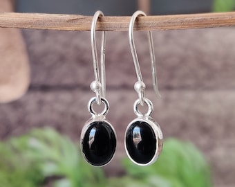 May include: A pair of silver dangle earrings with black oval gemstones. The earrings have a simple design and are perfect for everyday wear.