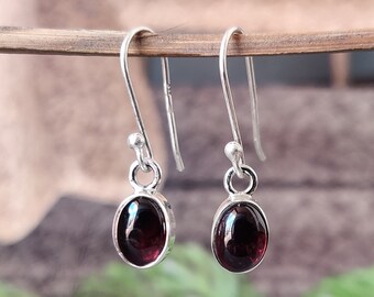 May include: A pair of silver dangle earrings with oval-shaped red garnet gemstones.