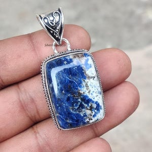 May include: A silver pendant with a blue and white lapis lazuli stone. The stone is rectangular and has a swirling pattern. The pendant is set in a silver frame with a decorative bail.
