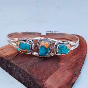 May include: Silver bangle bracelet with three turquoise stones set in silver. The stones are a mix of blue and orange.
