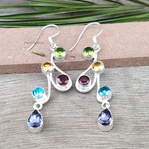 Puede incluir: Un par de pendientes de plata con un diseño curvo y múltiples piedras preciosas. Los pendientes presentan una amatista en forma de lágrima, una turquesa, un granate, una piedra amarilla y una piedra verde.