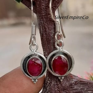 Può includere: Un paio di orecchini pendenti in argento con accenti di pietre preziose rosse. Gli orecchini presentano una pietra preziosa rotonda incastonata con un alone d'argento.