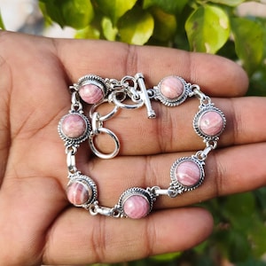 Könnte beinhalten: Ein silbernes Armband mit rosa und weißen gestreiften Steinen. Das Armband hat einen Schiebeverschluss.