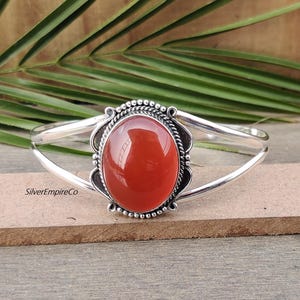 Può includere: Un braccialetto rigido in argento con una pietra di corniola arancione incastonata in una ghiera d'argento. La ghiera è decorata con un bordo di perline.