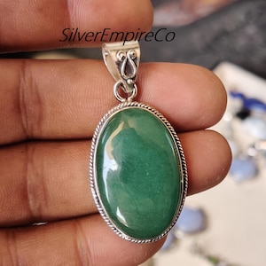 May include: A silver pendant with a green oval gemstone. The pendant has a detailed silver bail with a swirl design. SilverEmpireCo is printed on the image.