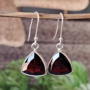 May include: A pair of silver dangle earrings with triangular red garnet gemstones.