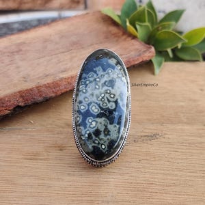 May include: A silver ring with a large oval-shaped black and white stone. The stone has a unique pattern of white spots on a black background. The ring is set in a silver band with a decorative edge.
