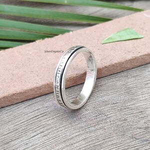 Puede incluir: Un anillo de plata con una banda texturizada y una línea negra alrededor del borde.