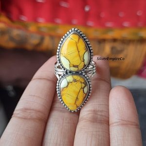 May include: A silver ring featuring two teardrop-shaped yellow stones with brown veining. The stones are set in a beaded bezel and connected by a silver band. The ring is a statement piece.