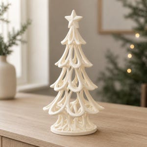 May include: A matte white decorative tree sculpture featuring an open, looped wire-like structure that forms tiered branches. The tree is topped with a five-pointed star and stands on a circular base, creating a hollow, airy silhouette.
