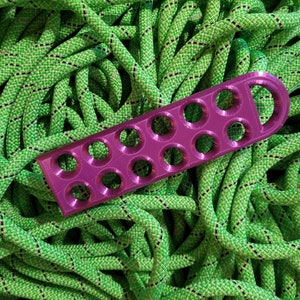 May include: A purple plastic climbing rope organiser with 10 holes. The organiser is lying on top of a pile of green climbing rope.