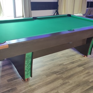 Peut inclure: Un billard avec un tapis vert, des bandes et des pieds en bois brun. Les pieds ont un motif décoratif avec des accents verts. Le billard est sur un sol en bois.