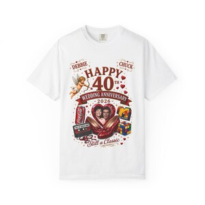 Op de afbeelding: Een wit t-shirt met een grafische print met de tekst Happy 40th Wedding Anniversary 2026, Debbie, Chuck en Still a Classic. Het ontwerp bevat een cupido, een Coca-Cola blikje, een cassettebandje, rode glitterhakken, een Rubik's kubus en een MTV-logo.