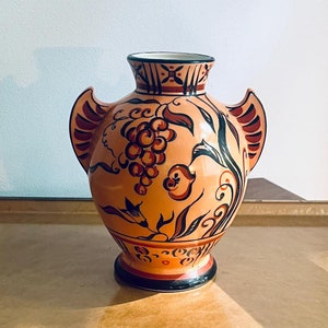 May include: A terracotta vase with black and red painted grape and floral designs. The vase has two handles and a rounded body.