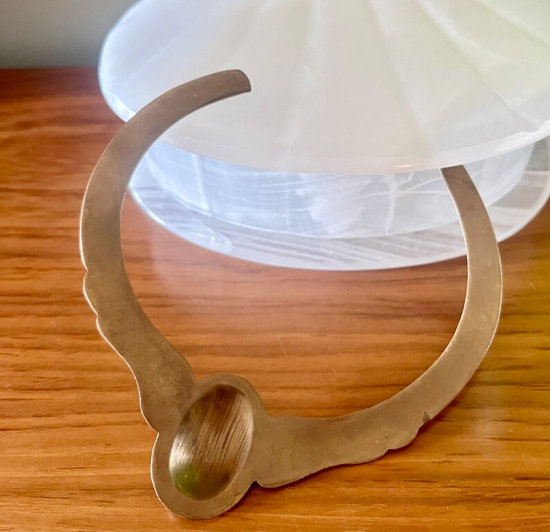 May include: A gold-toned metal bracelet with a large oval-shaped charm. The charm has a brushed finish and is set against a white background.