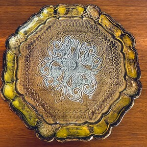 Pu&ograve; includere: Un vassoio decorativo dorato e verde con un design ornamentale. Il vassoio ha un bordo a festoni e un centro rialzato.