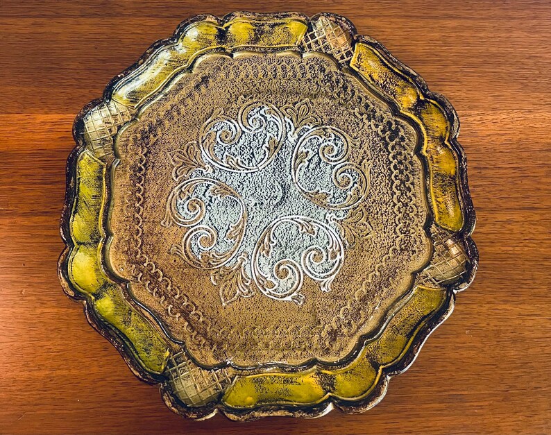 Pu&ograve; includere: Un vassoio decorativo dorato e verde con un design ornamentale. Il vassoio ha un bordo a festoni e un centro rialzato.