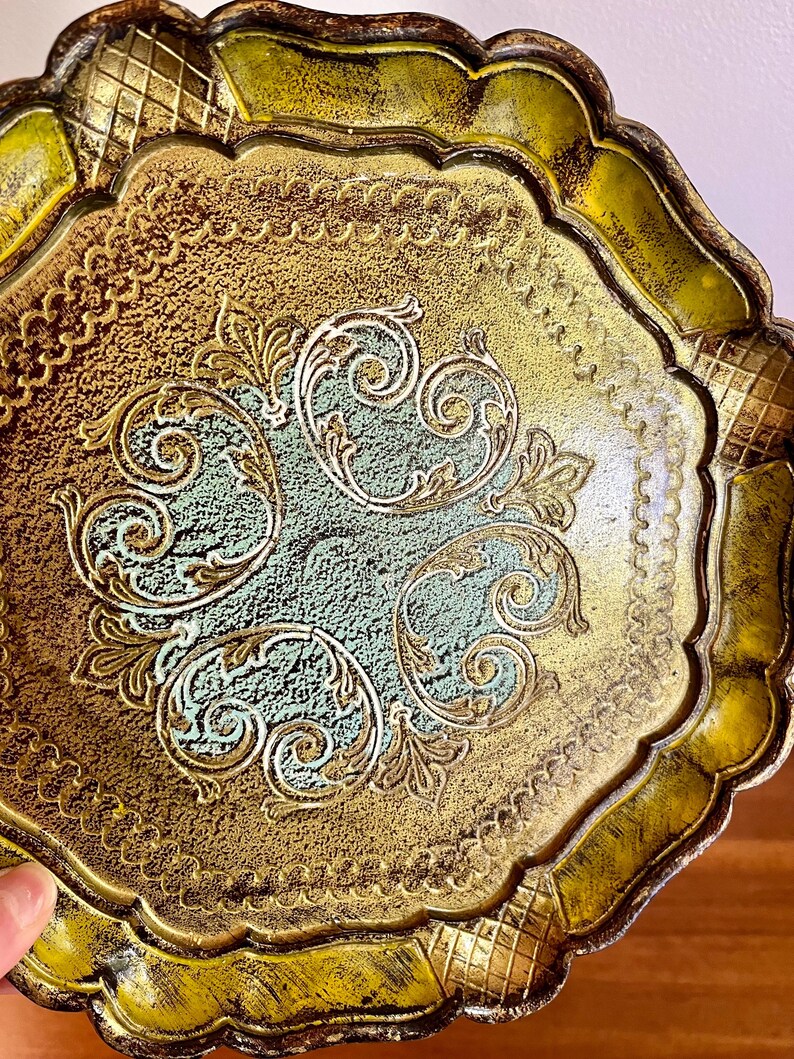 Pu&ograve; includere: Un vassoio decorativo dorato e verde con un bordo a festoni e un intricato disegno floreale.