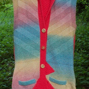 Puede incluir: Un chaleco sin mangas de punto con capucha, que presenta un patrón de degradado arcoíris y un panel frontal rojo. El chaleco tiene cierre de botones y dos bolsillos.