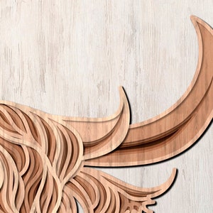 May include: A wooden cutout of a Highland cow with intricate layered details. The cow's head is facing the left side of the image, and the horns are curled up and out. The background is a light wood grain.