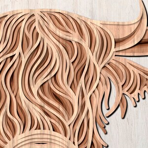 May include: A close-up of a wooden cutout of a Highland cow's head. The cutout is layered to create a 3D effect, with the fur of the cow being represented by intricate, layered lines.