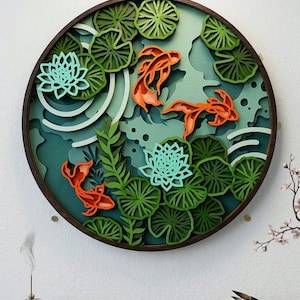 Peut inclure: Une œuvre d'art murale ronde en bois multicouche représentant des carpes koï orange nageant parmi des nénuphars verts et des fleurs de lotus turquoise. L'œuvre est placée sur un fond bleu et vert d'eau, encadrée par une bordure en bois brun foncé. L'ensemble évoque la sérénité.