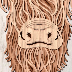 May include: Close-up of a wooden cutout of a Highland cow's face. The cow's fur is made of layered wood, creating a 3D effect. The cow's nose and eyes are visible.