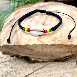 May include: A black cord bracelet with a white seashell charm and red, yellow, and green beads.