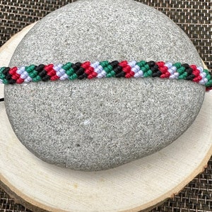 May include: A green, white, black, and red friendship bracelet made with woven string.