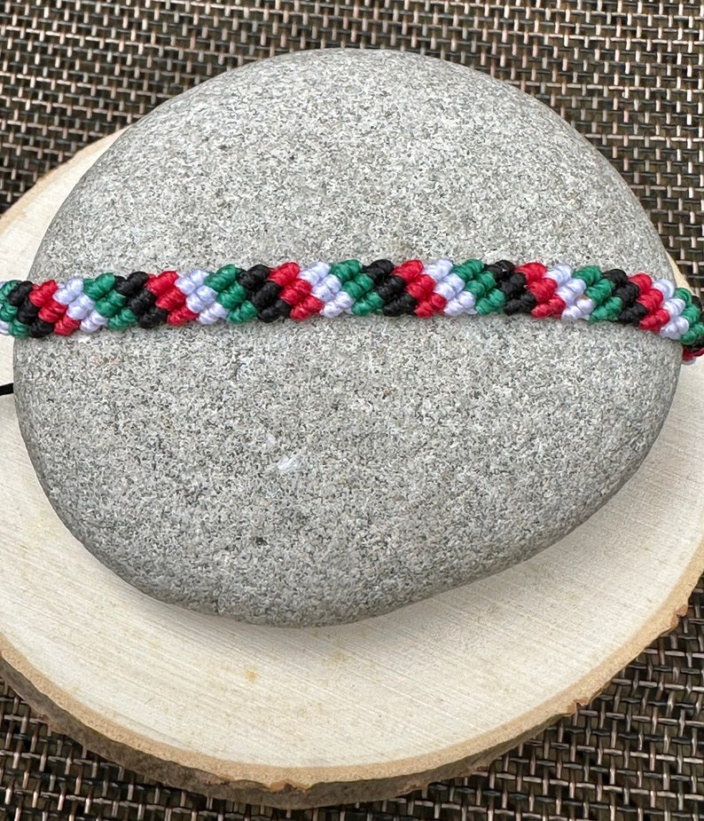 May include: A green, white, black, and red friendship bracelet made with woven string.