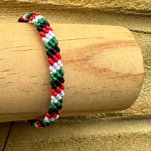 May include: A braided bracelet with red, white, green, and black stripes. The bracelet is made of woven string and is a popular style of friendship bracelet.