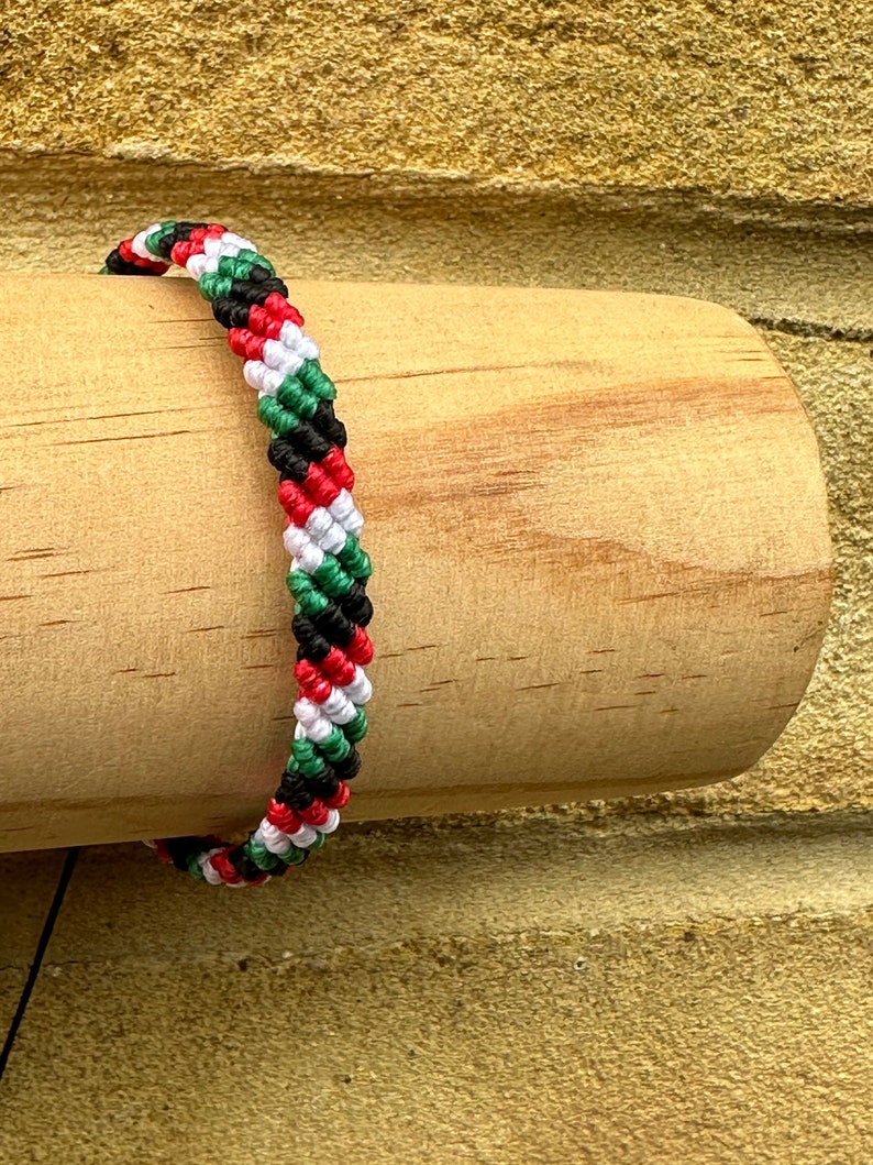May include: A braided bracelet with red, white, green, and black stripes. The bracelet is made of woven string and is a popular style of friendship bracelet.