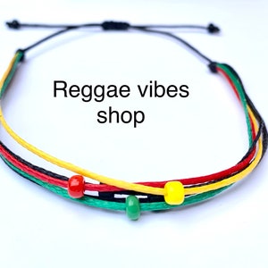 Puede incluir: Un brazalete de cuerda multicolor con cuerdas rojas, amarillas, verdes y negras. El brazalete tiene tres pequeñas cuentas, una roja, una amarilla y una verde.
