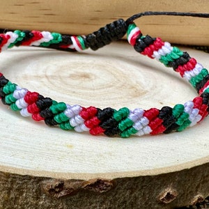 May include: A braided friendship bracelet with red, white, green, and black stripes. The bracelet is made of woven string and has a simple knot closure.
