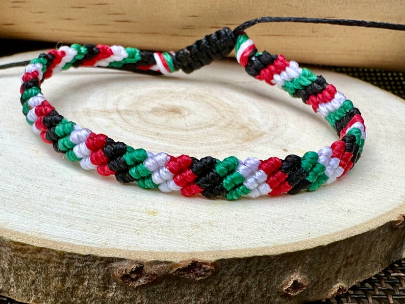 May include: A braided friendship bracelet with red, white, green, and black stripes. The bracelet is made of woven string and has a simple knot closure.