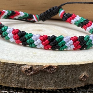 May include: A braided friendship bracelet with red, white, green, and black stripes. The bracelet is made of woven string and has a simple knot closure.