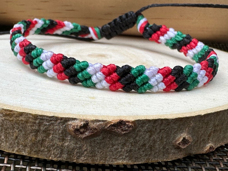 May include: A braided friendship bracelet with red, white, green, and black stripes. The bracelet is made of woven string and has a simple knot closure.