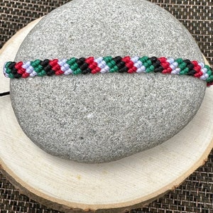 May include: A black, red, white, and green friendship bracelet with a braided pattern.
