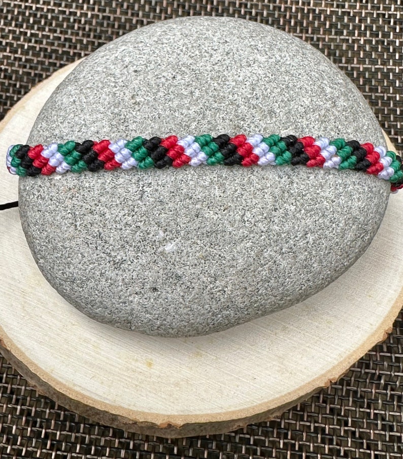 May include: A black, red, white, and green friendship bracelet with a braided pattern.