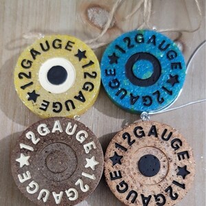 May include: Four circular ornaments with the text "12 GAUGE" and star accents. The ornaments are in yellow, blue, brown, and tan. Each has a central circle in a contrasting color. They are connected by a string.