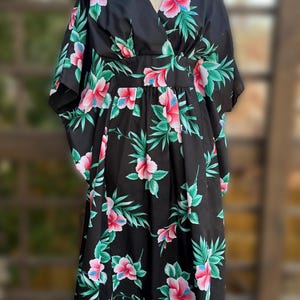 May include: Black dress with a floral pattern of pink hibiscus flowers and green leaves. The dress has a V-neck, short sleeves, and a fitted waist. The fabric looks lightweight. The dress is displayed on a mannequin, suitable for warm weather.