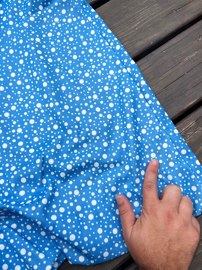 Puede incluir: Una tela azul con un patr&oacute;n de lunares blancos. La tela est&aacute; doblada y una mano la est&aacute; tocando.