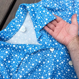 Puede incluir: Un vestido azul con lunares blancos, cuello y cierre de bot&oacute;n. El vestido est&aacute; hecho de una tela suave y ligera.