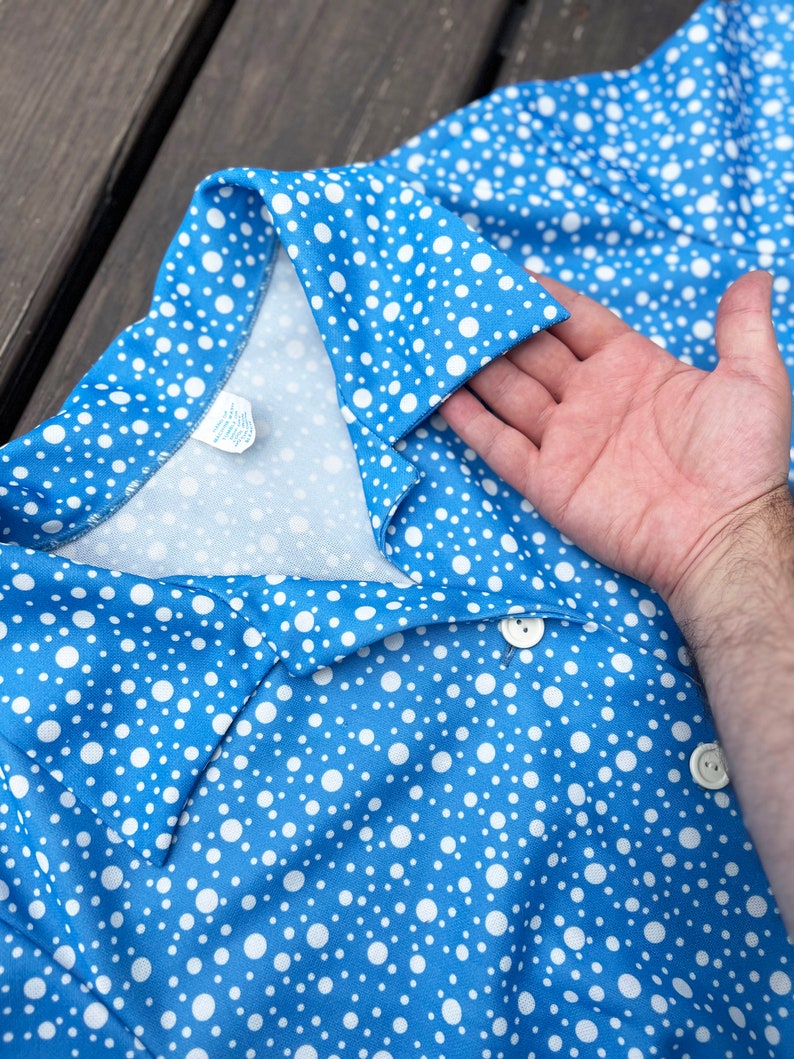 Puede incluir: Un vestido azul con lunares blancos, cuello y cierre de bot&oacute;n. El vestido est&aacute; hecho de una tela suave y ligera.