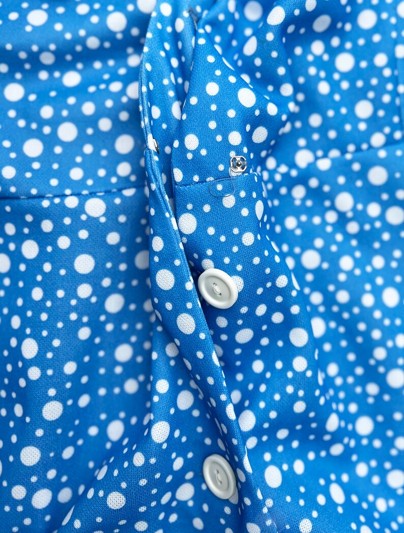 Puede incluir: Primer plano de una tela azul con lunares blancos. La tela tiene una costura en el centro con dos botones blancos.
