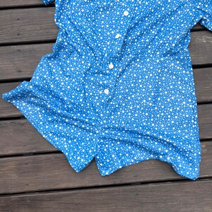 Puede incluir: Un mono de manga corta azul y blanco con lunares, cuello y cierre de botones.