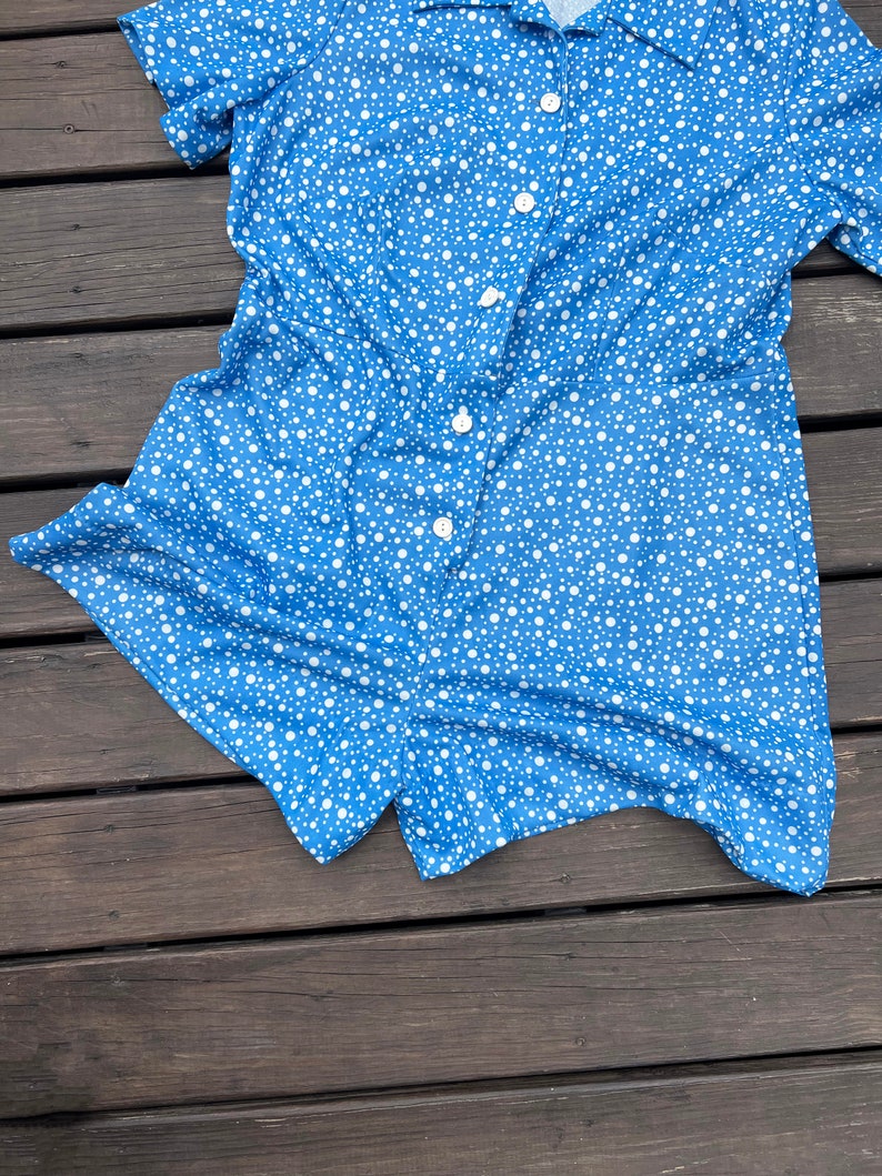 Puede incluir: Un mono de manga corta azul y blanco con lunares, cuello y cierre de botones.