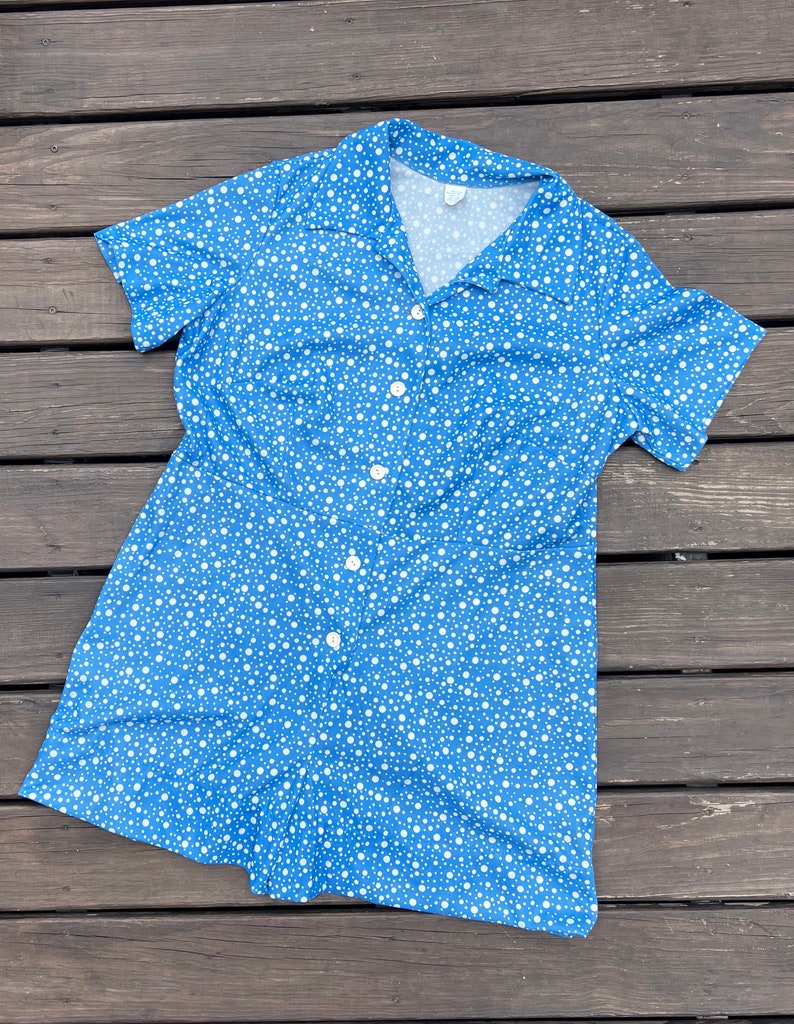 Puede incluir: Un vestido azul y blanco de lunares con botones y manga corta.