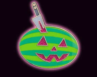 May include: An oval enamel pin featuring a green and lime striped watermelon shaped like a jack-o'-lantern. The face has triangular eyes and a jagged mouth filled with pink glitter. A silver-toned knife is embedded in the top of the fruit.