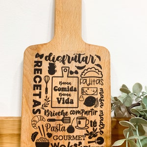 Könnte beinhalten: Ein Schneidebrett aus Holz mit einem braunen Holzgriff und einem schwarzen Design mit den Worten "disfrutar", "recetas", "buena comida", "buena vida", "fajitas", "brioche", "compartir", "pasta", "te", "masa madre", "gourmet", "wok" und "pizza".